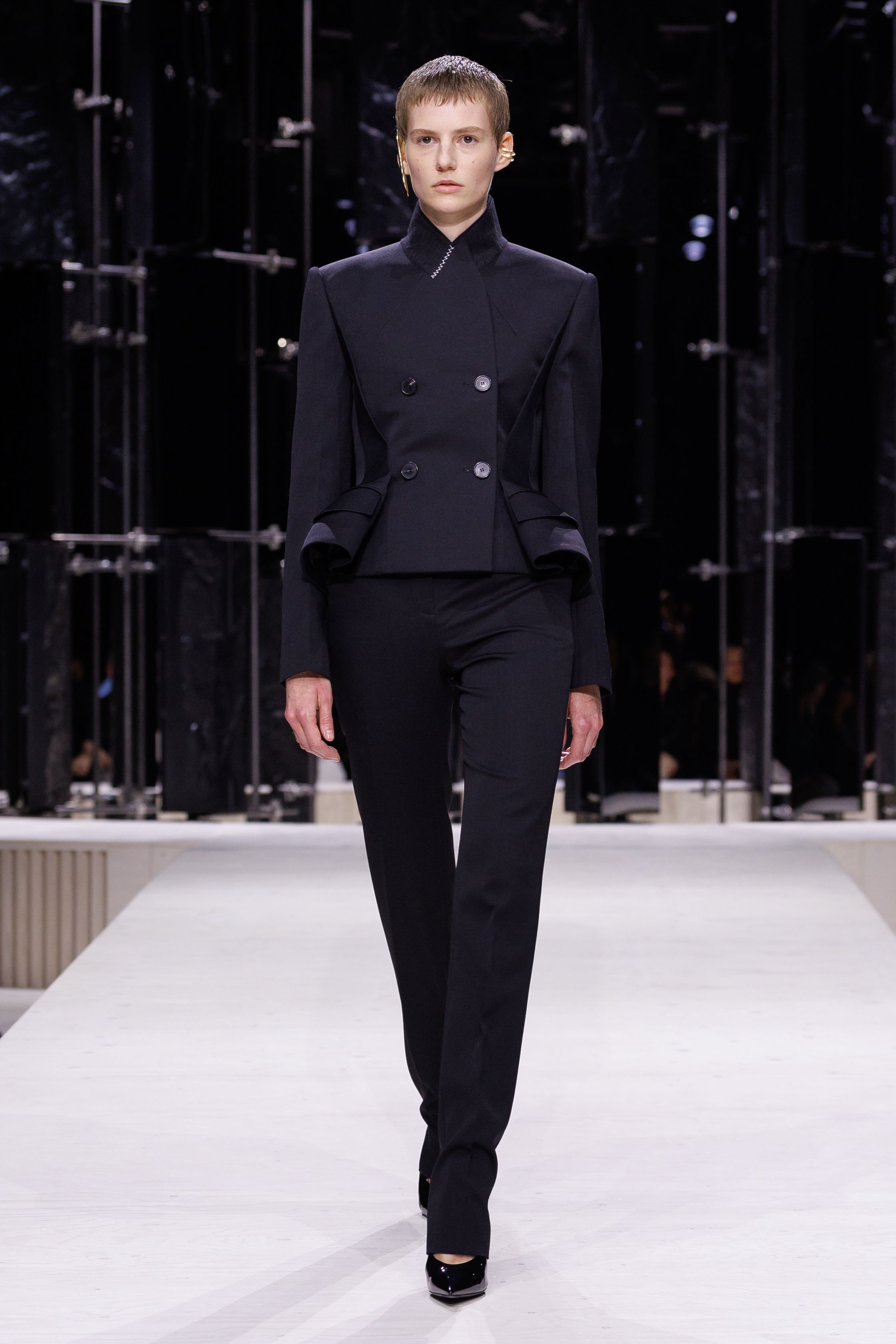 Givenchy 2026秋冬在现代建筑空间中呈现一场充满戏剧性的时装叙事：雕塑式西装、亮色斗篷、结构礼服与夸张装饰共同构建品牌标志性的高级时装气质。蓝色、红色与黄色的高饱和色彩与黑白经典形成鲜明对比，服装通过立体剪裁与夸张廓形展现出强烈视觉张力。整场系列在优雅与戏剧之间取得平衡，展现现代高级时装的力量-顽石频道趋势研究